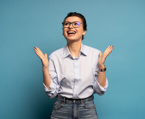 Extremely happy woman standing with raised clenched fists, winning lottery, celebrating her success isolated on blue
