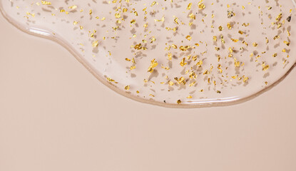 Serum fluid 24k gold gel facial cream smear, on beige pastel background. Beauty cosmetic product smudge, pure transparent lotion with gold particles, skin care jelly serum, top view Luxury moisturizer