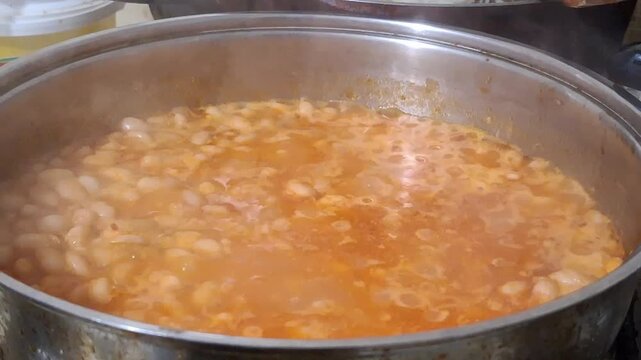 Close up of traditional Turkish white bean stew (Kuru Fasulye) simmering in a metal pot on a kitchen stove