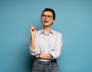 Enthusiastic middle aged woman, entrepreneur points up, eureka gesture, has an idea, on blue background
