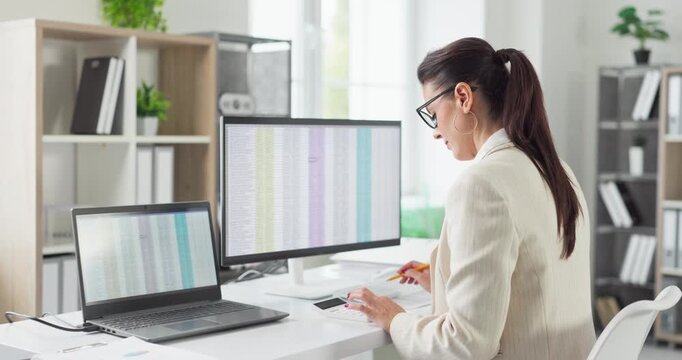 Accountant woman auditor in office, finance analysis. She checks spreadsheet data on computer using a calculator to verify bookkeeping accuracy and compliance. Solid audit control concept theme.