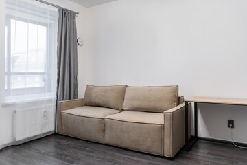 stylish studio apartment with minimalist design. gray curtains on large window, a beige sofa near the wall, and a bedside table. The apartment has white walls and a dark floor.