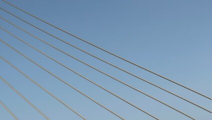 Obraz premium Parallel steel cables of a suspension bridge stretch across a clear blue sky