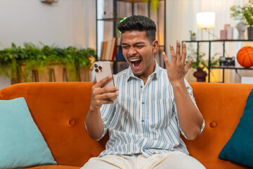 Indian man at home scrolls smartphone feed sees sale news and says wow smiles enjoy discount deals....
