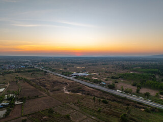 Aerial sunrise view of rural transportation infrastructure, featuring a road cutting through countryside landscape with warm golden light, natural surroundings, and village settlement.