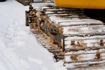 Industrial excavator track detail showing metal track plates with snow and mud buildup demonstrating heavy machinery movement on cold outdoor work site
