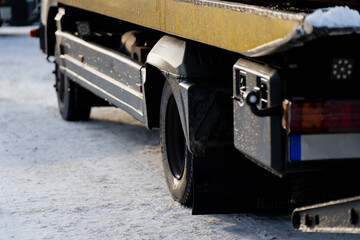 Rear section of flatbed work truck showing mudguard wheel and side storage box parked on snowy ground highlighting commercial vehicle detail and winter operation conditions