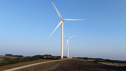 Two wind turbines on green field, and blue sky