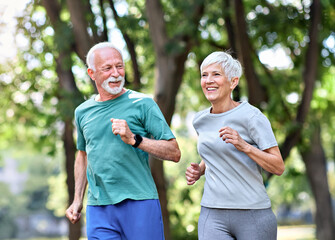 Smiling active mature senior couple jogging together in the park