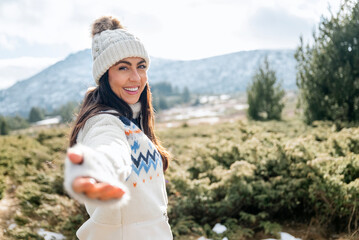 Beautiful smiling woman looking at the camera with outstretched hand in the winter mountain 
