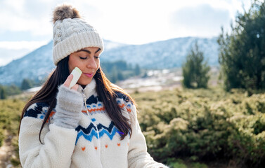 Beautiful woman applying sunscreen stick  in the winter mountain