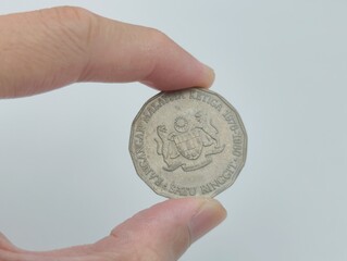 Vintage Malaysian one ringgit coin showing national coat of arms, held between fingers for scale. © abgmohdariff