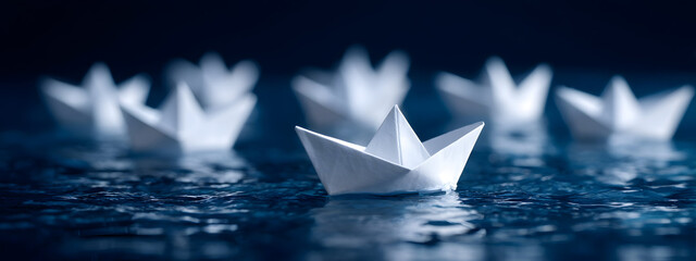 A leading paper boat confidently guides its small fleet across a shimmering, deep blue surface, representing unity, aspiration, and navigating the journey ahead