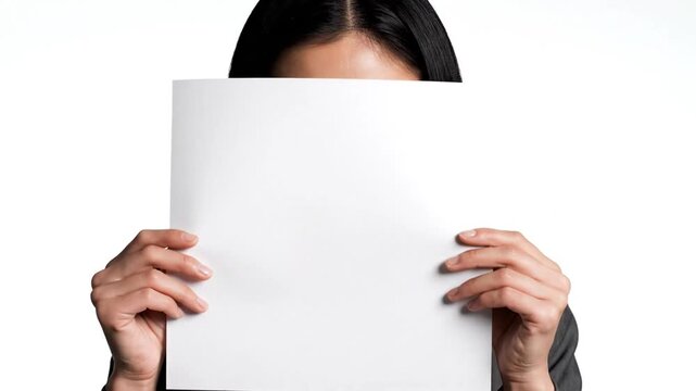 Cinematic slow motion portrait of an elegant Asian business woman hiding her facial expression behind a blank white paper sheet in a minimalist professional setting.