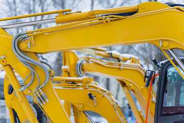 Close up of yellow construction excavator booms and hydraulic systems aligned in work yard highlighting heavy machinery structure engineering and winter operation setup