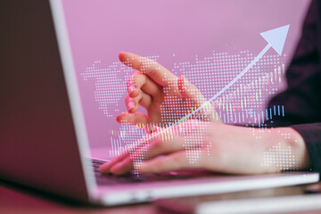 Hands on laptop keyboard with digital world map and upward trend graph during late evening hours in a workspace setting