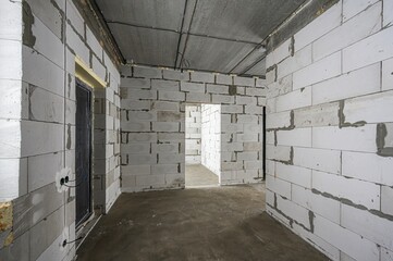 Unfinished room with aerated concrete block walls, exposed concrete ceiling, concrete floor. Metal door installed, open doorway to adjacent space, visible mortar joints