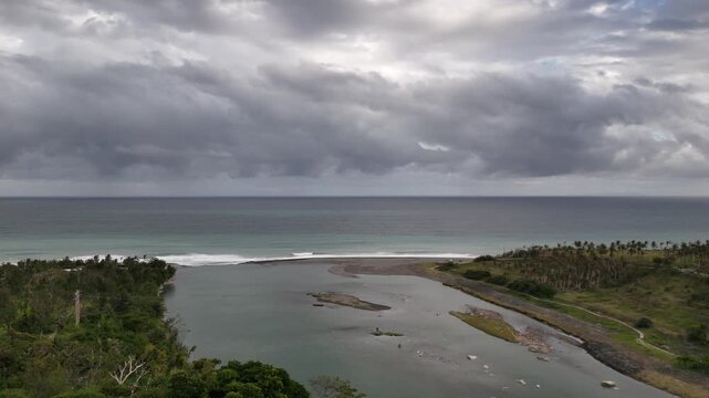B roll of a moody coastline under dark storm clouds where a river meets the grey blue ocean framed by sandy beaches lush vegetation and tropical palms