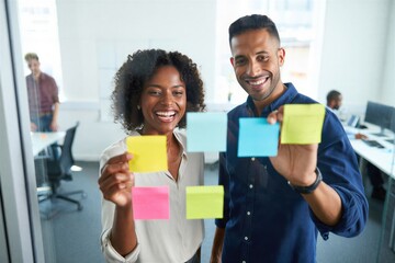 A diverse team collaborates on a project using colorful sticky notes on a glass wall. Creative teamwork and idea generation.