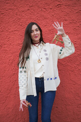Ukrainian woman in traditional embroidered clothing standing against a red textured wall and holding handmade straw ornaments, including didukh elements, representing Ukrainian folk culture, heritage,