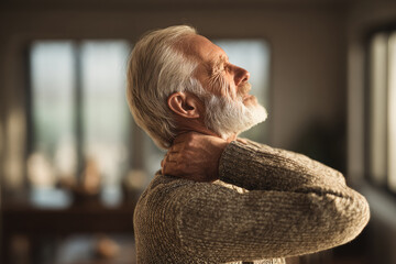 Elderly man experiencing muscle inflammation in neck area, conceptual image showing discomfort and pain in home environment with warm natural light and thoughtful expression