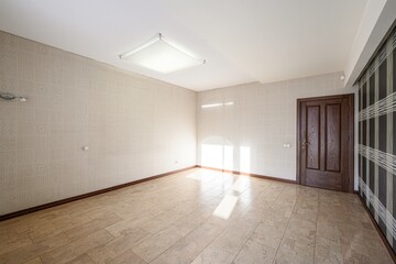 Obraz premium Spacious unfurnished room with beige patterned wallpaper, tiled floor, wooden door, recessed ceiling light, natural light from window, dark paneled section on one wall. Clean, modern look