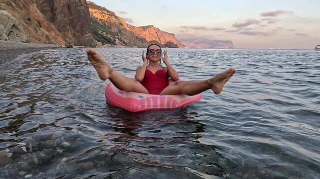 Woman donut sea, happy woman relaxing on donut float in the sea near rocky beach at sunset