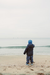Child standing on a beach looking at the ocean on a cloudy day