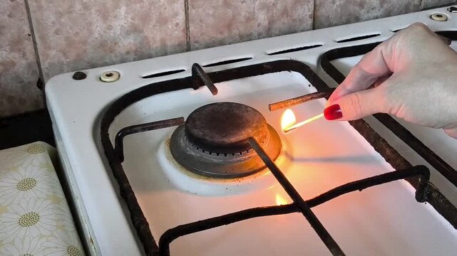 A woman brings a burning match to the gas and turns on the gas burner of the stove in the kitchen. Gas consumption, price increases