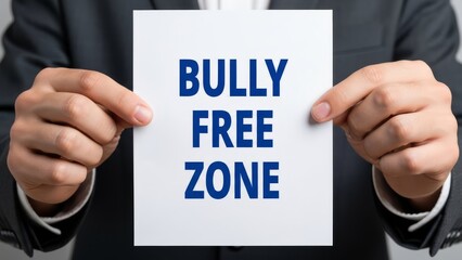 Hands holding a white paper sign with blue text reading 'BULLY FREE ZONE' to promote safety and wellbeing