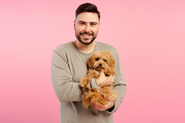 Portrait of smiling bearded man holding fluffy dog looking at camera isolated on pink background
