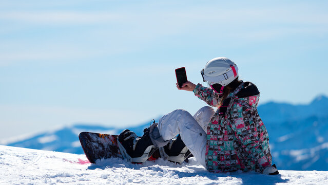 Girl (woman) with snowboard deck and equipment deating and making selfie on the phone on the top of the snow peak of alps mountains in Italy during winter day light