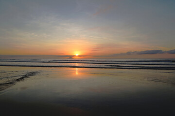 A wide view of the sky with golden reflections on Itaguare beach in Bertioga, Brazil at dawn.