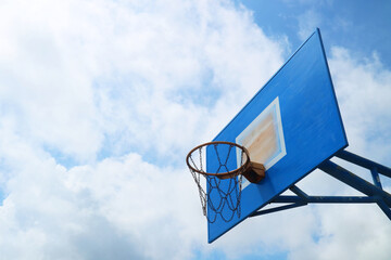 Outdoor basketball hoop and blue backboard against a bright blue sky with white fluffy clouds. © Reza
