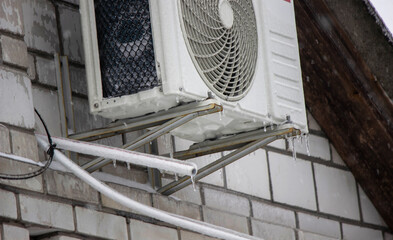 Icy air conditioner and power lines after freezing rain. Winter weather emergency.