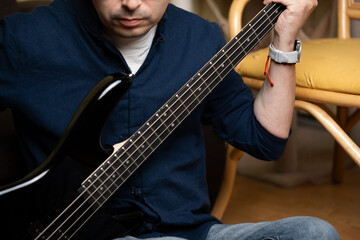 Middle aged man practicing scales on black electric bass guitar at home, Close up of musician hands...