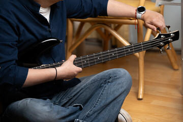 Musician tuning a black electric bass guitar before a practice session, Close up of hands adjusting tuning pegs on a bass guitar headstock