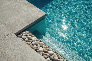 Close-up of pool's edge concrete steps, pebble-filled border, shimmering water