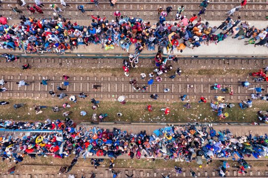 Tongi, Bangladesh - 12 January 2020: Aerial view of vibrant crowds thronging railway platforms and tracks, a sea of colorful clothing contrasting with the brown earth.