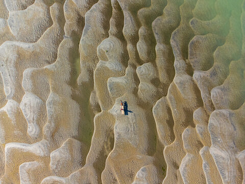 Gaibandha, Bangladesh - 14 December 2025: Aerial view of a lone figure contrasting against the vast, rippled sand expanse, creating a mesmerizing pattern of light and shadow near the river bank.