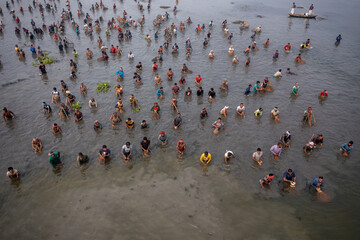 Pabna, Bangladesh - 05 December 2020: Aerial view of people wading in the shallow, reflective waters, their figures creating a mosaic of humanity against the muted tones of the landscape.