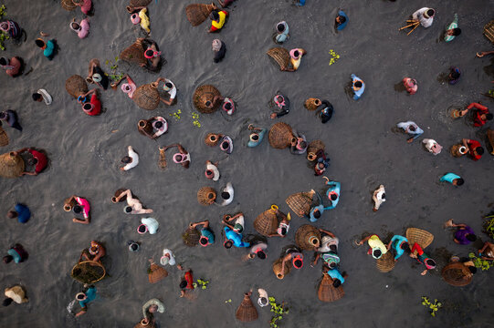 Pabna, Bangladesh - 05 December 2020: Aerial view of people wading through muddy waters, their colorful clothing a stark contrast to the monochrome landscape.