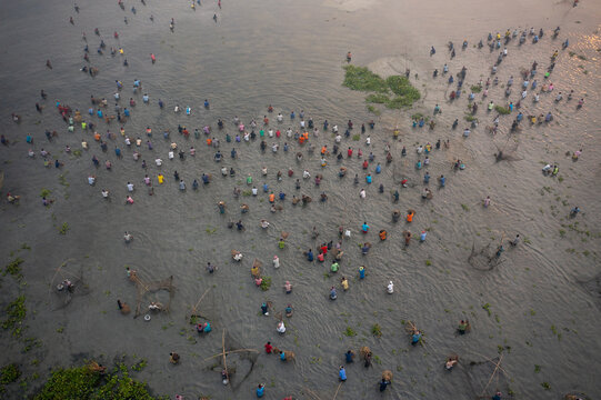 Pabna, Bangladesh - 05 December 2020: Aerial view of a bustling crowd congregating on the muddy banks, their colorful clothing creating a vibrant mosaic against the stark, grey landscape.
