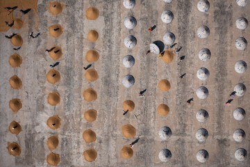 Brahmanbaria, Bangladesh - 29 October 2021: Aerial view of golden and silver mounds of grains scattered across a vast concrete expanse, with dark silhouettes of people and birds.