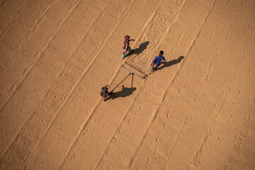 Brahmanbaria, Bangladesh - 29 October 2021: Aerial view of workers carefully tending to the golden grains spread across the field, creating a mesmerizing pattern.