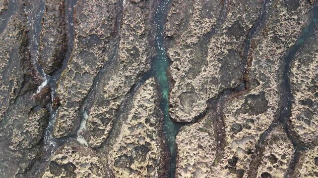 B roll of eroded coastal rock with flowing seawater revealing grooves textures and patterns that symbolize memory time harmony and tension in a poetic natural shoreline scene