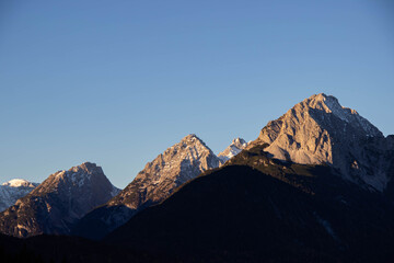 Fototapeta premium Majestic mountain peaks illuminated by golden sunlight, showcasing rugged terrain and snow-capped summits against a clear blue sky, embodying the beauty of nature's landscape