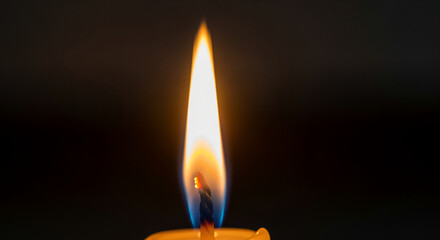 A single candle flame burns brightly against a dark background creating a warm and cozy ambiance with a yellow and blue fire with warmth and peaceful