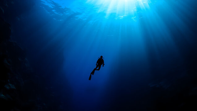 Scuba diver exploring ocean depths with sunbeam shining through water