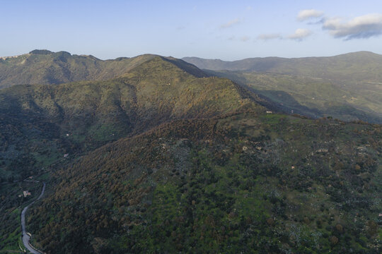 Aerial view of the rugged, verdant slopes meeting the sky, a tapestry of light and shadow cascading across the mountainous terrain, Botindari, Sicily, Italy.